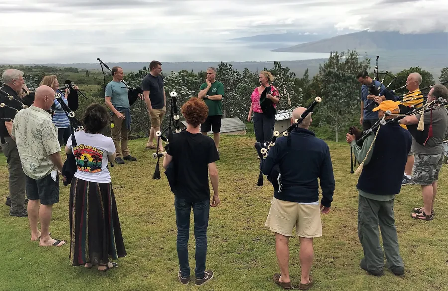 A practice circle of pipers on a lawn above the ocean