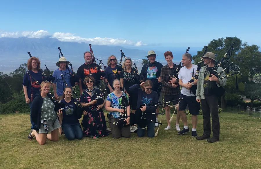 Students holding pipes on a hillside with the ocean behind